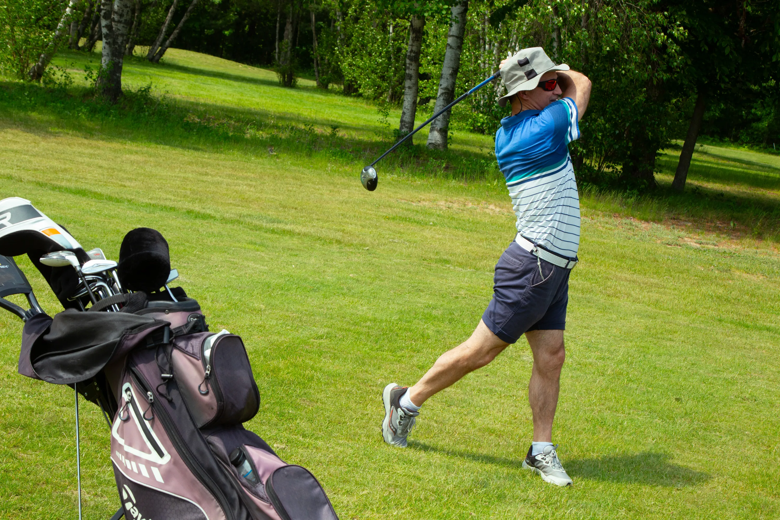 Golfeur en pleine extension après un élan, avec son sac de bâtons à ses côtés sur le champ de pratique
