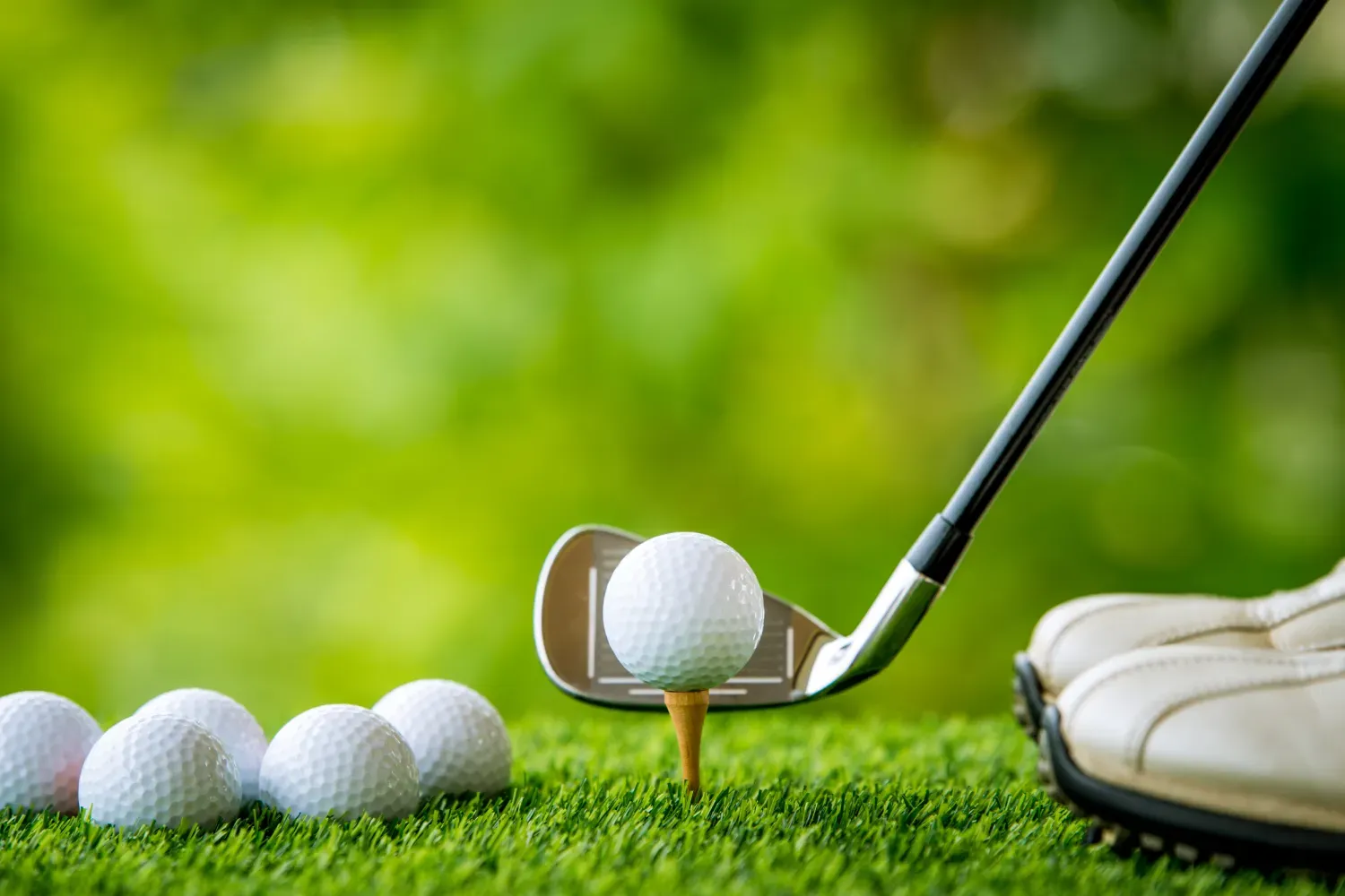 Balle de golf posée sur un tee devant un fer, avec plusieurs balles alignées au premier plan — leçon privée